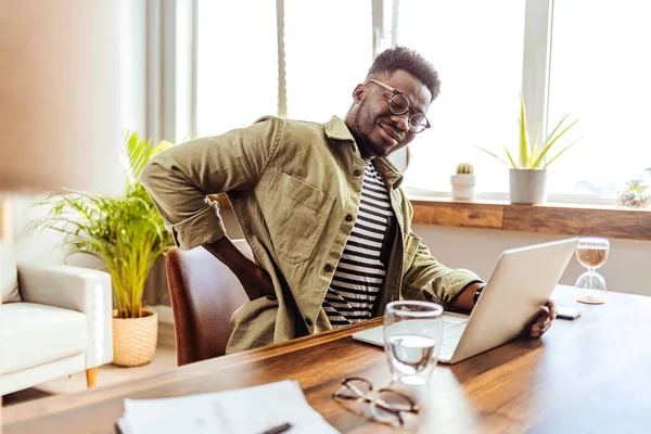 Masasında çalışırken sırtı ağrıyan genç bir iş adamının görüntüsü. Ofisinde masasında çalışırken sırt ağrısı çeken genç bir işadamı..