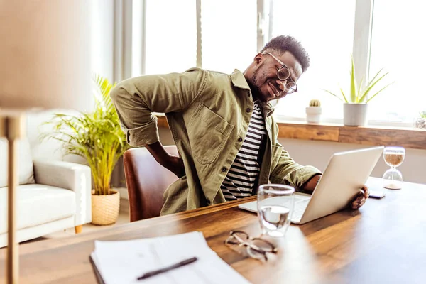 Sırtımda ağrı var. Afrika kökenli Amerikalı adam sırt masajı yaptırıyor belinde ağrı var modern ofiste işyerinde oturmaktan acı çekiyor. Lumbar Ache. Sağlık Sorunu Konsepti.