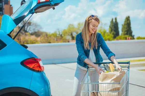 Genç bir kadın alışveriş malzemelerini arabaya yüklüyor.