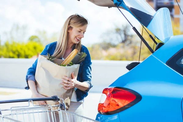 Genç bir kadın alışveriş malzemelerini arabaya yüklüyor.