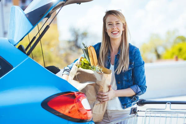 Genç bir kadın alışveriş malzemelerini arabaya yüklüyor.