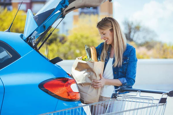 Genç bir kadın alışveriş malzemelerini arabaya yüklüyor.