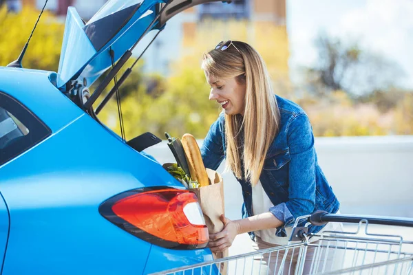 Genç bir kadın alışveriş malzemelerini arabaya yüklüyor.