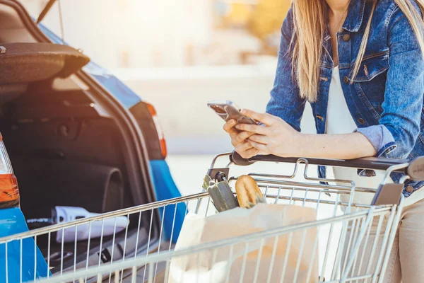 Young Woman Shopping Cart Smartphone Standing Car — стоковое фото