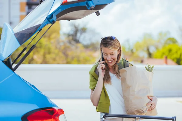路上で食料品を手に買い物袋を持ちながら携帯電話で話す若い女性 — ストック写真