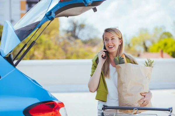 路上で食料品を手に買い物袋を持ちながら携帯電話で話す若い女性 — ストック写真