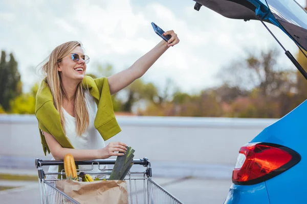 路上でスマホで自撮りするショッピングカートを持った若い女性 — ストック写真