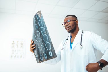 Young doctor looking at computed tomography x-ray image. Confident pleasant doctor working with MRI scan results. Radiologist man checking x-ray, health care, medical and radiology concept