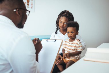 Shot of a single mother bringing his little boy for a checkup. Happy multiracial family visiting clinic for check up. Kind male pediatrician smiles as he talks with an adorable baby boy.