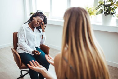 Professional psychotherapies and young woman suffering from ptsd. The teenage girl sits hopelessly with her head resting on her hand as she listens to advice from the unrecognizable mature adult female counselor.