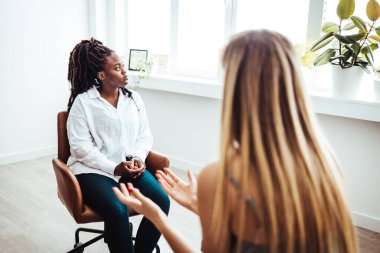 Professional psychotherapies and young woman suffering from ptsd. The teenage girl sits hopelessly with her head resting on her hand as she listens to advice from the unrecognizable mature adult female counselor.