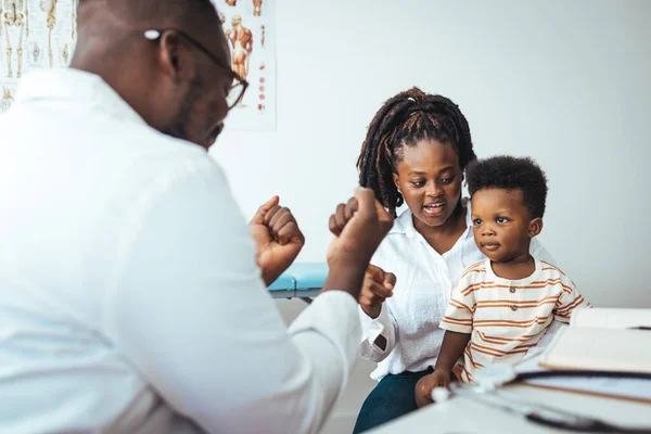 Smiling caring male pediatrician talk consult small boy patient at consultation in hospital with mother. Happy doctor do checkup examine little child at visit to clinic with mom. Healthcare concept.