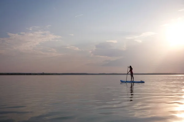 Silhouette de jeune femme paddle boarding au coucher du soleil. — Photo