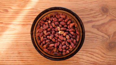 Kabukta kızarmış fıstık, ahşap zemin üzerinde beyaz cam tabakta soyulmuş yer fıstığı..