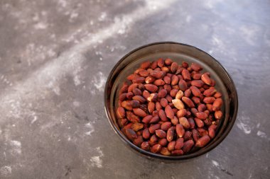 Kabukta kızarmış fıstık, koyu ahşap masada beyaz cam tabakta soyulmuş yer fıstığı..