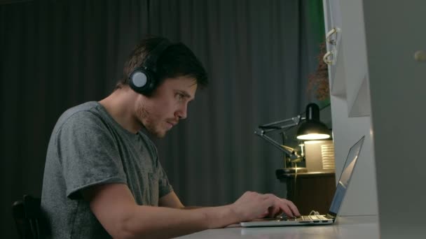 Чоловік в розчісуванні позиції слухати музику на навушниках використовують ноутбук вночі . — стокове відео