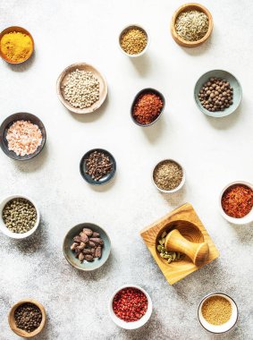 Küçük kaselerde çeşitli kuru baharatlar ve gri arka planda havan topu düzlüğü vardı. en üstteki görünüm