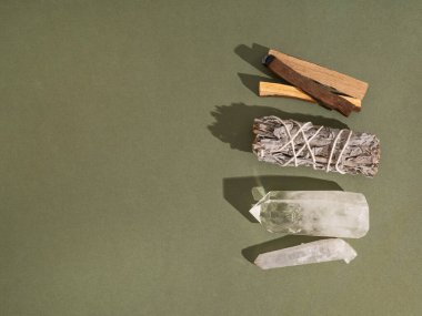 Ruhani temizlik için malzemeler, adaçayı, palo santo tütsü çubukları ve yeşil arka planda kuvars kristali. Üst Manzara. Boşluğu kopyala