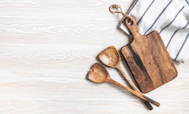 Kahverengi kesim tahtası, aletler ve pamuk peçeteyle en az ahşap mutfak arka planı. Mutfak gereçleri beyaz sehpada. Boşluğu kopyala, üst görünüm