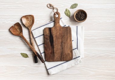 Kahverengi kesim tahtası, çeşitli baharatlar, aletler ve pamuk peçeteyle minimum ahşap mutfak arka planı. Mutfak gereçleri beyaz sehpada. Boşluğu kopyala, üst görünüm