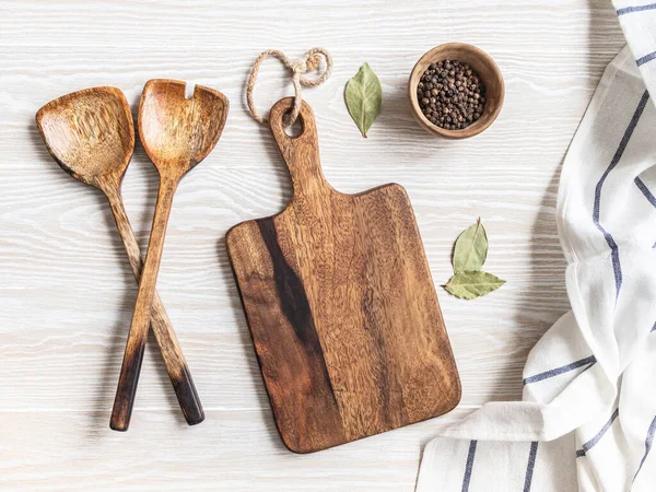 Kahverengi kesim tahtası, çeşitli baharatlar, aletler ve pamuk peçeteyle minimum ahşap mutfak arka planı. Mutfak gereçleri beyaz sehpada. Boşluğu kopyala, üst görünüm