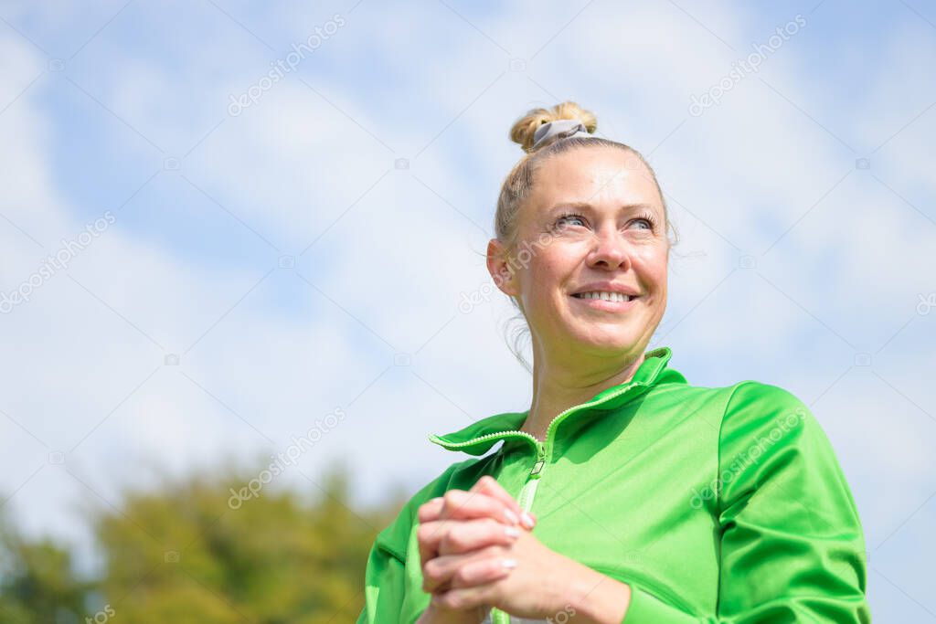 Happy woman with a positive attitude outdoors in sunshine in a low angle view as she looks off to the side with a smile while clasping her fingers