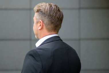 Beyaz gömlek ve ceket giyen, özgüvenli, yakışıklı, orta yaşlı bir adamın arka plan portresi fotokopi alanı için gri duvara yaslanmış.