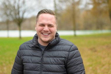 Sonbaharda sıcacık bir ceketle parkta dikilirken kameraya sırıtan mutlu genç adam.