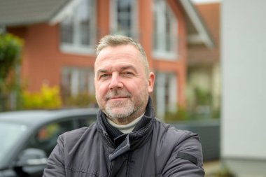 Sıcak ceketli bir adam kışın şehir sokağında poz veriyor. Sessiz, düşünceli bir gülümsemeyle kameraya bakıyor.