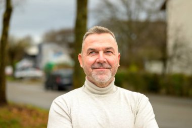 Düşünceli bir adam, sonbaharda bir şehir caddesinde sakin bir gülümseme ve zevk ile yukarı bakıyor.