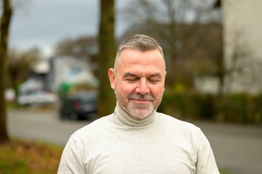 Kapalı gözlerle rahatlayan bir adam ve mutlu bir gülümsemeyle bir şehir sokağında kafa ve omuzlarda bir portre