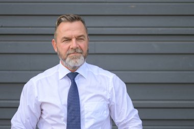 Yoğun orta yaşlı işadamı, gri bir dış duvara karşı ön kafa ve omuz portresiyle düşünceli bir şekilde yan tarafa bakıyor.