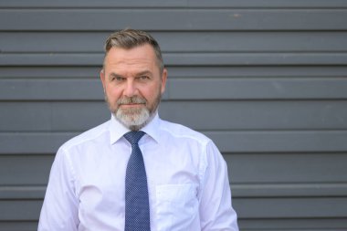 Yoğun orta yaşlı işadamı, gri bir dış duvara karşı ön baş ve omuz portresiyle düşünceli bir şekilde kameraya bakıyor.