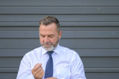 Akıllı sakallı, orta yaşlı bir adam gri bir duvara kelepçelerini baş ve omuz portresiyle takıyor.