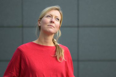 Düşünceli sarışın kadın, kafasında derin bir ifadeyle fotokopi alanı olan gri bir duvara bakıyor.