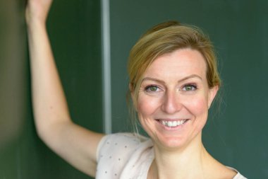 Close-up portrait of female teacher in class writing on the chalkboard Today lesson and looking to the camera with friendly face clipart
