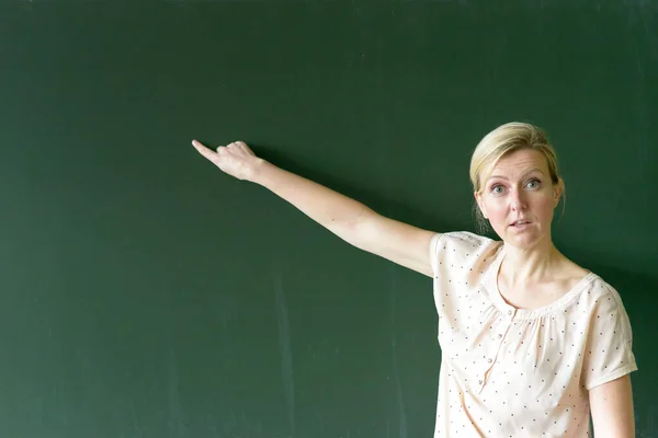 Lehrerin Zeigt Mit Verdutztem Blick Auf Leeren Kopierraum Auf Kreidetafel — Stockfoto