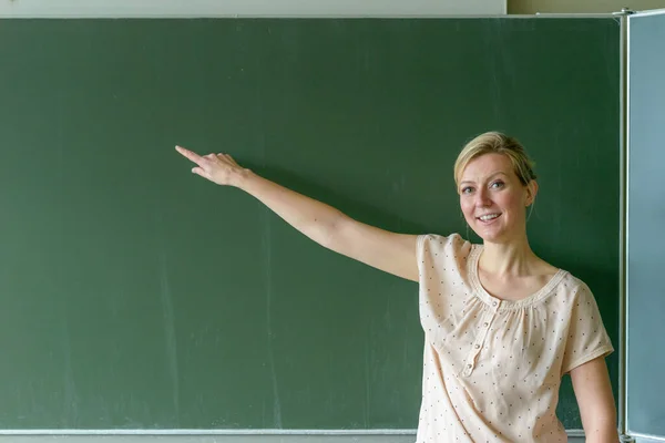 Nauczycielka Wskazująca Miejsce Tablicy Patrząc Kamerę Uśmiechając Się — Zdjęcie stockowe