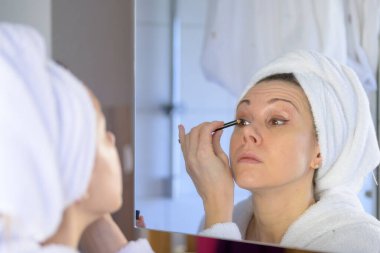 Banyodaki aynaya göz kalemi süren orta yaşlı bir kadın güzellik ve tımar konseptine odaklanıyor.