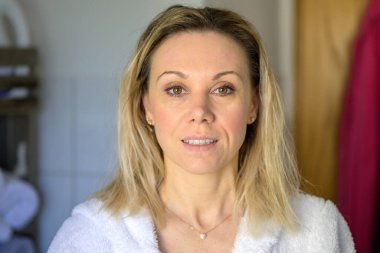 Açık tenli, banyo cüppeli, gülümseyen yetişkin kadın portresi.