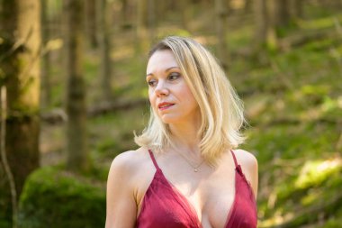 Baştan çıkarıcı sarışın kadın. Şehvetli mor elbiseler giyiyor. Ormanda dalgın dalgın dalgın dalgın bakıyor.