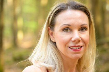 Ormanda açık kahverengi gözlü, gülümseyen sarışın güzel bir kadının yakın plan portresi.