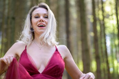 Alçak açılı, sarı saçlı, seksi mor elbiseli neşeli bir kadın portresi. Ormanda keyifli bir hafta sonu geçiriyor.