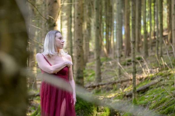 Baştan çıkarıcı sarışın kadın ormanda ağaçların arasında dikilirken gözlerini kaçırıyor.