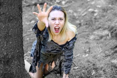 Kederli kadın çığlık atıyor ve kameraya uzanıyor. Orman zemininde çömelirken elleriyle tırmalıyor.