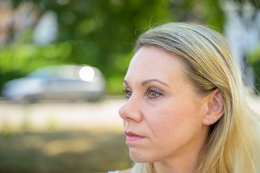 Düşünceli, orta yaşlı bir kadının, sakin bir şehir sokağında dışarı bakarken çekilmiş fotoğrafı.