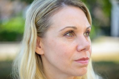 Düşünceli sarışın kadın yan tarafa bakıyor. Yakın çekimde açık havada bir sorun yaşıyor.