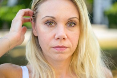 Düşünceli orta yaşlı bir kadın, düşünceli bir yüz ifadesiyle, yakın plan bir vesikalık fotoğrafta yan tarafa bakıyor.