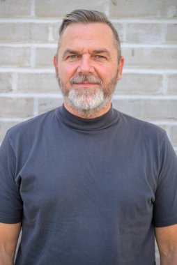 Ciddi sakallı son sınıf öğrencisi, üst vücut portresiyle kameraya dikkatlice bakıyor.