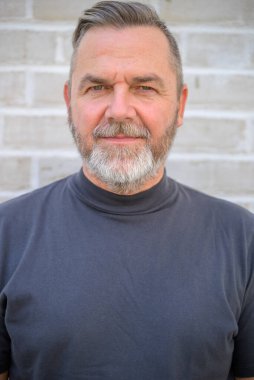 Ciddi orta yaşlı bir adam yakın planlanmış bir portrede kameraya dalgın dalgın bakıyor.